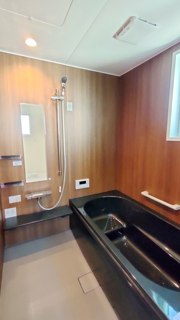 浴室は３面に木目調パネルを貼り、黒いシックな高断熱浴槽に断熱フタでお湯が冷めにくい